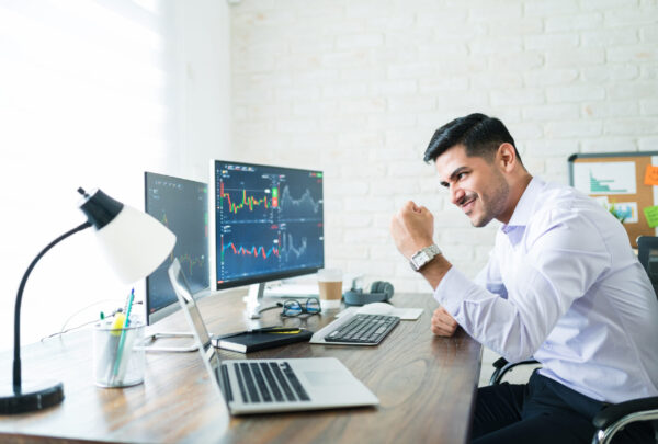 Confident handsome Hispanic financial broker showing fist to computer screen while trading from home