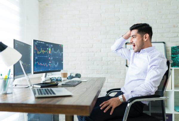 Surprised young Latin freelance trader sitting with mouth open while looking at graphs on computer screens